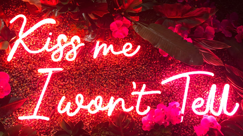 Neon sign that reads "Kiss me I won't tell" on outside wall