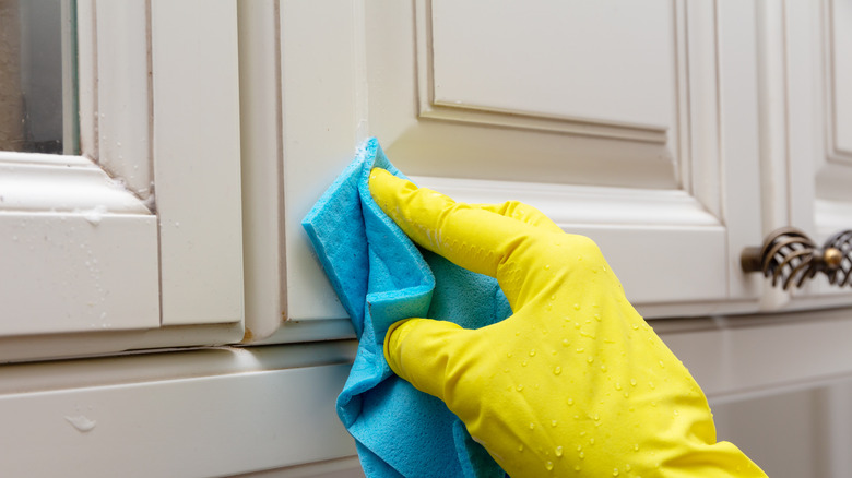 gloved hand wiping kitchen cabinets