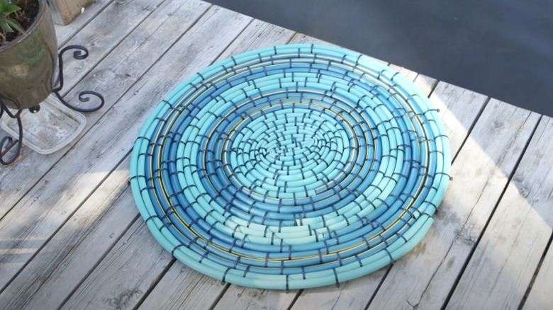 A blue-green circular floor mat made out of a garden hose