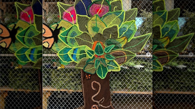 Colorful tree and butterfly crochet ornament on a chain link fence