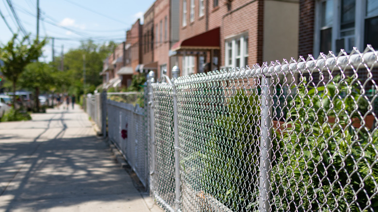 Sidewalk view of rowhouses with a plain chain link fence