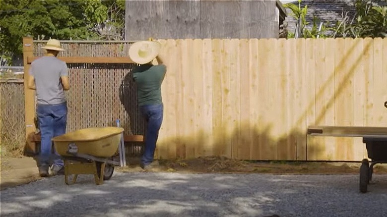 Men covering chain link fence with wood planks