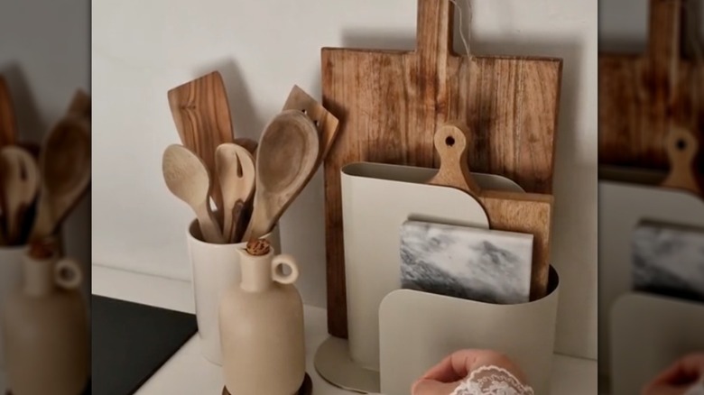 Hand stirs a drink next to cutting boards stored in file organizer on beige countertop