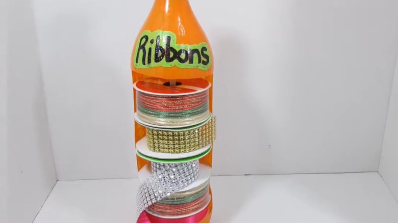 Bright orange soda bottle holding spool of ribbon