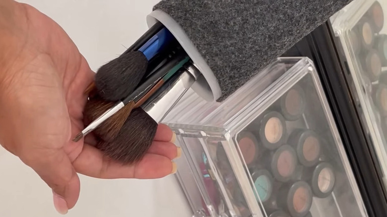 Hand holding makeup brushes out of repurpose drink mix container