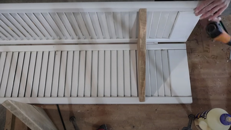 Someone building a corner shelf with white shutters