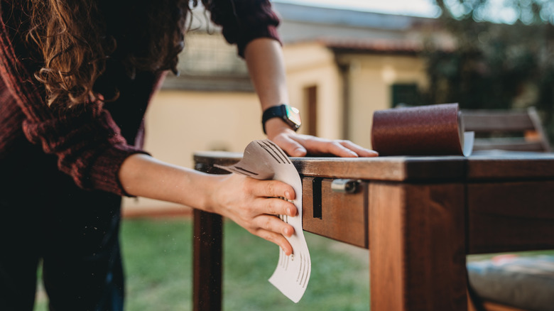 person sanding an old dining table outside to prepare for reuse