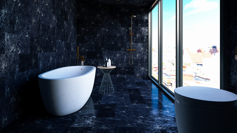 Black marble tiled bathroom with white bathtub and large window