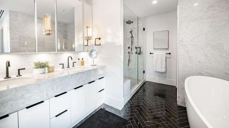 Black marble herringbone tiles on bathroom floor with white marble walls and vanity