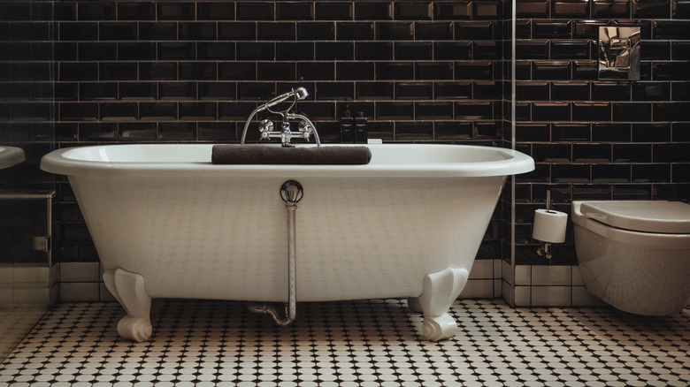 Black tiled wall behind white tub with white and black flooring