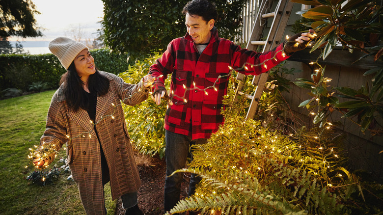 couple hanging Christmas lights outside