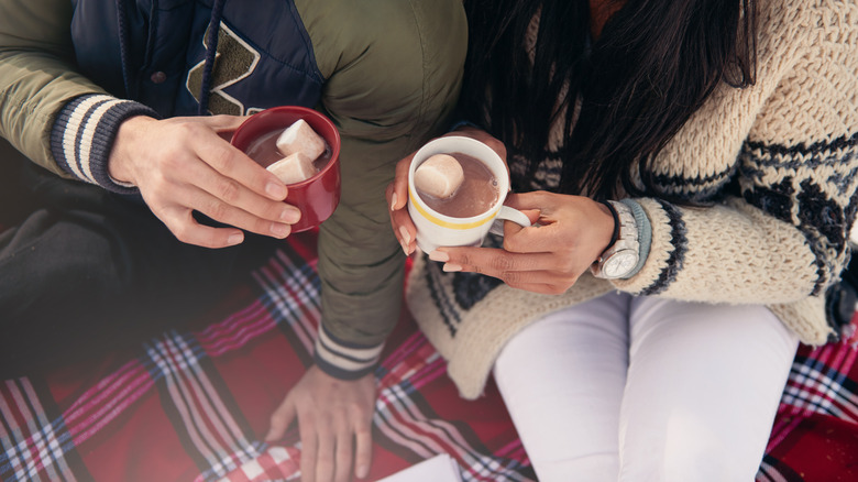 Hands holding mugs over blanket