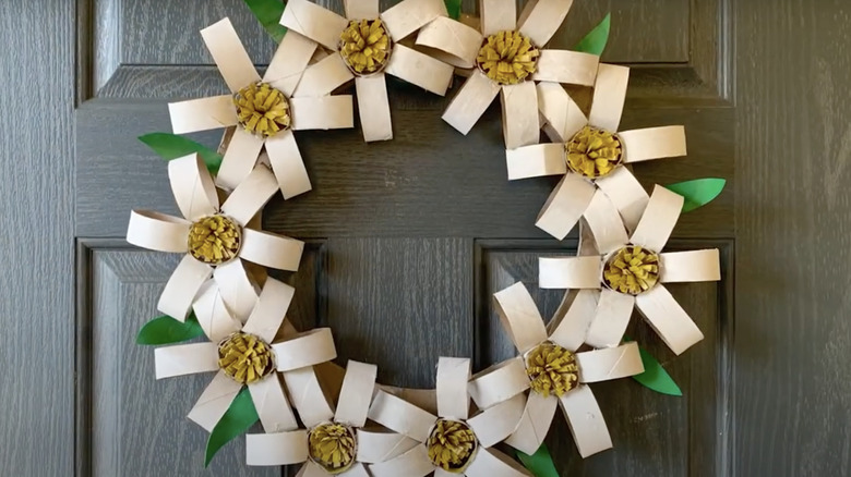 A wreath made of cardboard toilet paper roll daisies and painted white, yellow, and green.