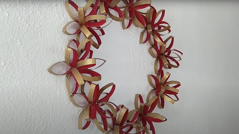 A three dimensional flower wreath made from empty toilet paper rolls and painted red and gold.