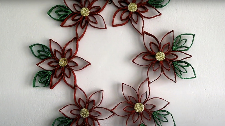 A festive wreath featuring glittery paper poinsettia flowers and leaves.