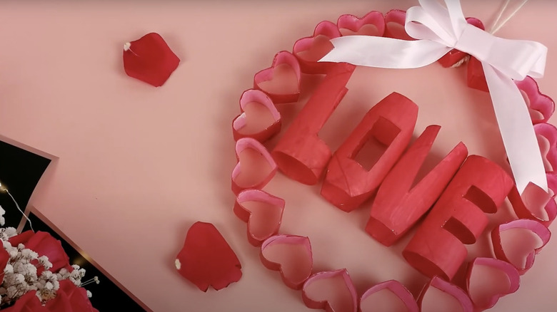 A wreath made from toilet paper rolls fashioned into hearts with a white ribbon bow and the word love inside.