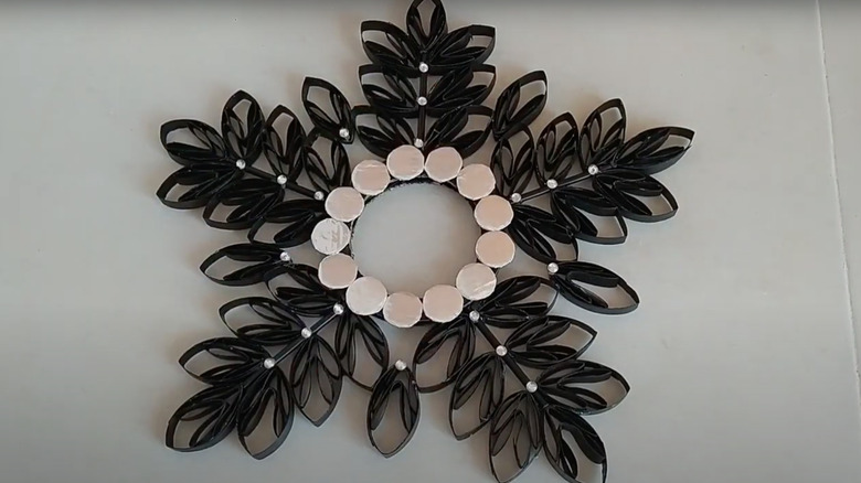 A monochromatic wreath featuring black-painted cardboard branches with leaves, silver discs, and pearls.