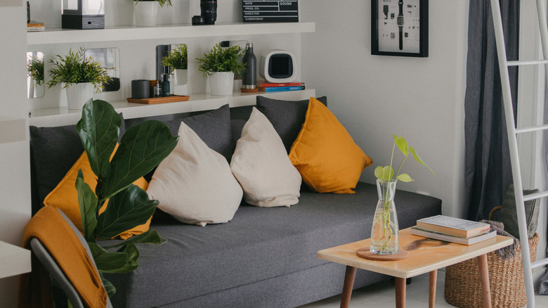 A small space with a grey couch and bright yellow pillows.