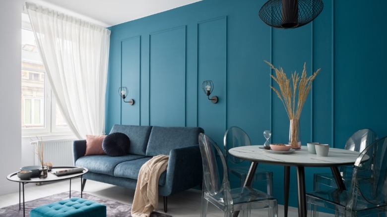 A boldly-styled room with a teal wall, dark gray couch, and a chic table and an open window.