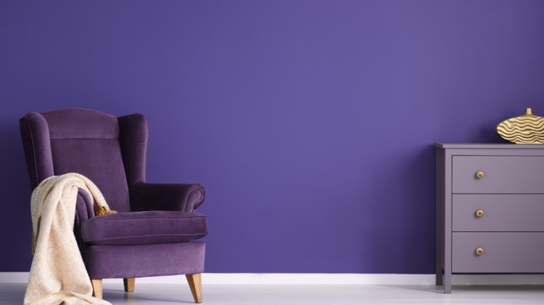 A purple armchair against a dark purple wall with a purple cabinet to the side