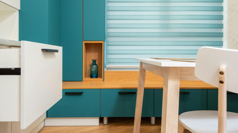 A modern home interior with bright teal cabinets next to light-colored cabinets and table