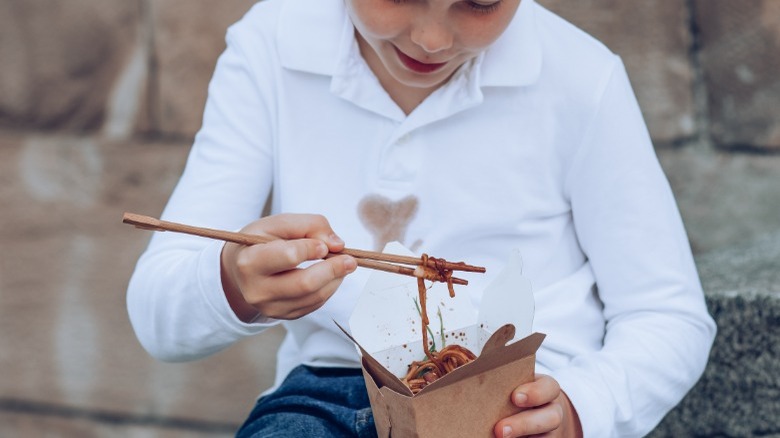 Boy eating lo mein, grease stain on shirt