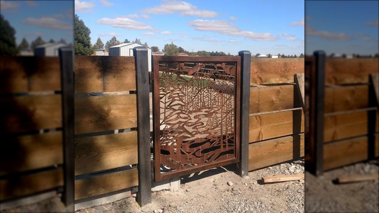 Wooden fence with a metal fence gate with designs cut out of it