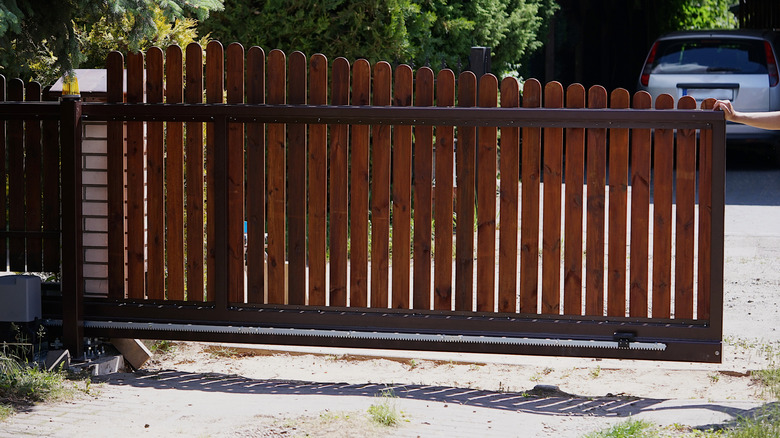 Partially open wooden sliding fence gate that a person is touching