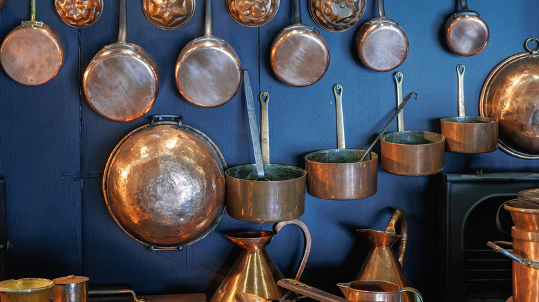 Copper pots hang on a deep blue wall.