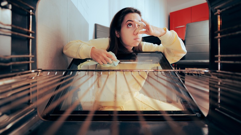 Woman holding her nose cleaning the oven