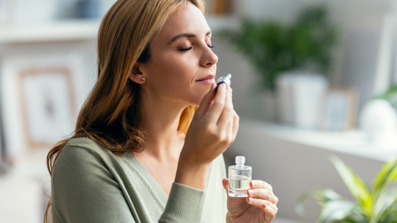 A woman holds and smells perfume sample in her home