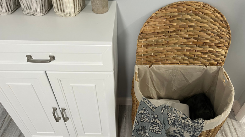 An open laundry hamper next to a shelf in a laundry room