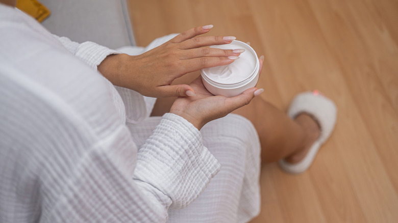 A person in a bath robe holds a jar of body lotion