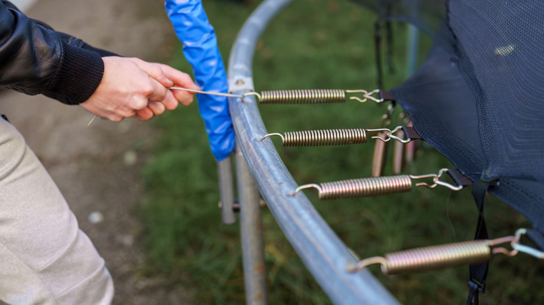 A man pulls on a trampoline spring to remove it from the metal frame.