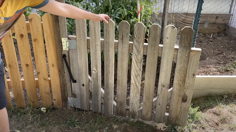 A woman pulls a gate toward her to demonstrate how the spring she installed helps it close automatically.