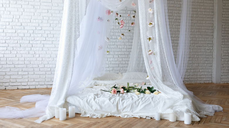 Mattress on the floor with a lace canopy above and flowers