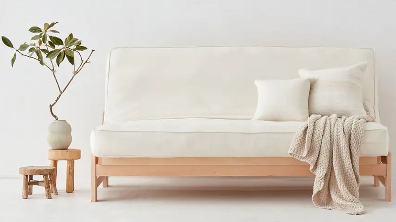 Futon with light wood base set up like a couch with plant beside it