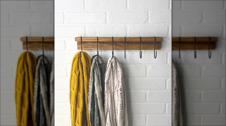 Wooden rack on a white wall that has scarves hanging from S-hooks on it