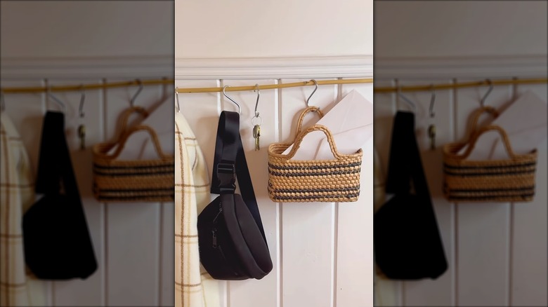 Thin wooden rod on the wall with S-hooks hanging supporting keys, purses, and other items