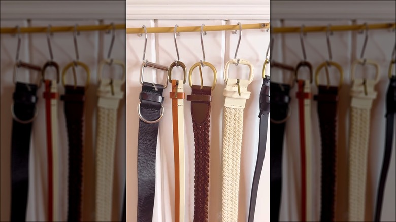 Thin wooden rod on a wall with S-hooks on it that are hanging belts