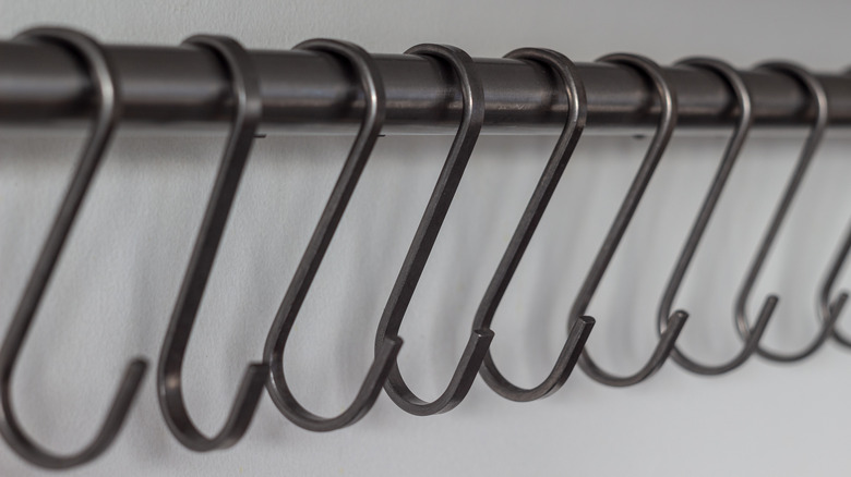 Row of S-hooks hanging on a rod with a white wall in the background