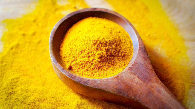 A wooden spoon with a scoop of tumeric spice