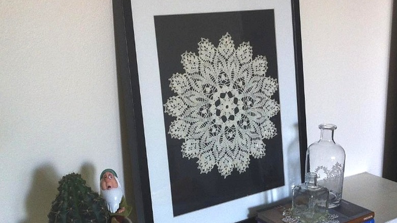 Framed and matted doily on console table with vases and other decorations