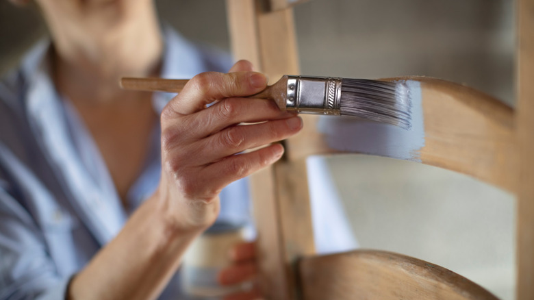 Woman painting a wooden chair with gray paint