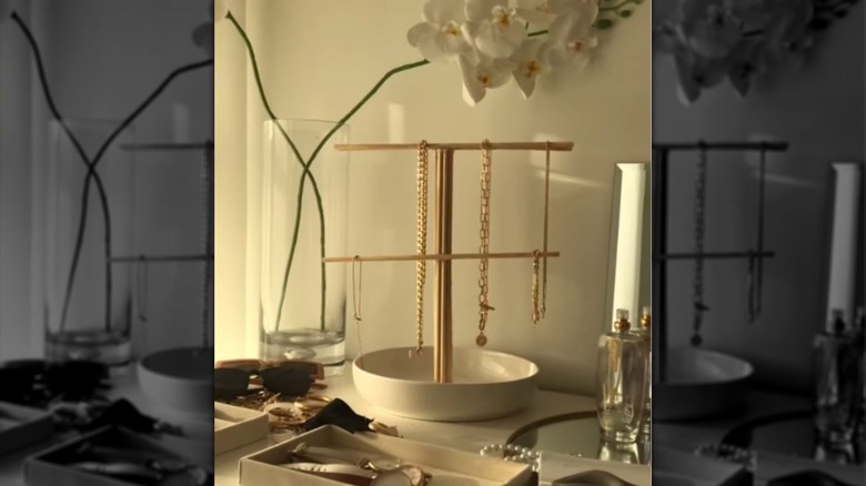 A golden jewelry stand made from wooden rods holding delicate necklaces and bracelets on a countertop.