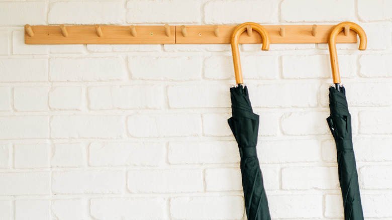 Two umbrellas hang from a wooden wall mounted coat rack..