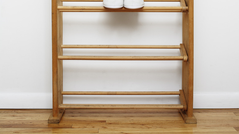 A wooden shoe rack with a white pair of tennis shoes resting on wooden dowels.