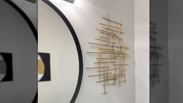 An interesting wall decor piece is assembled using small wooden rods painted gold.