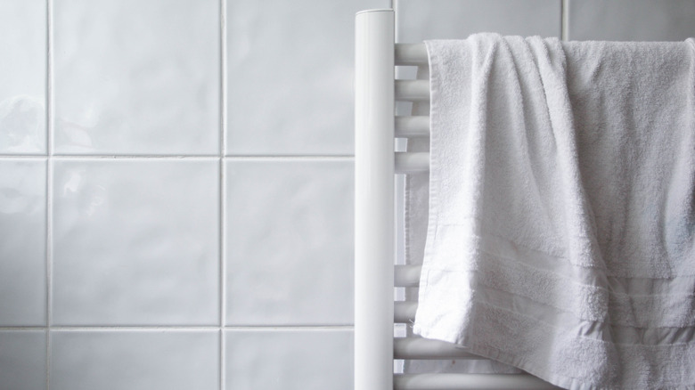 A white towel hangs on a towel rack made of wooden dowels against a tiled wall.