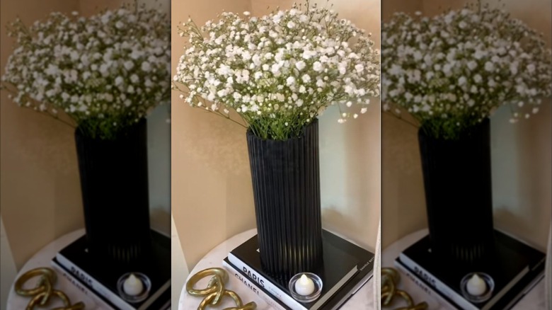 A black vase made from wooden dowels holds lovely white blooms.